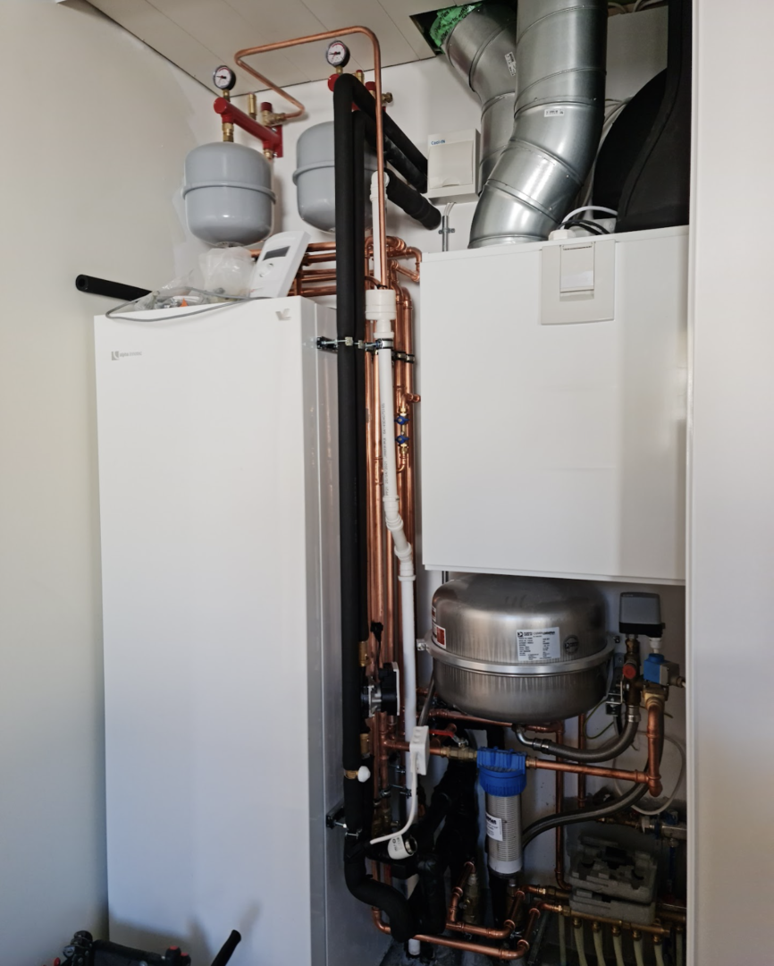 A white and ympäristöystävällinen heating system installation with metal pipes, gauges, and a water tank in a utility room.